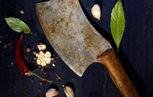 Sharp butcher knife lying on butcher block with vegetables. Whetstone sharpening.